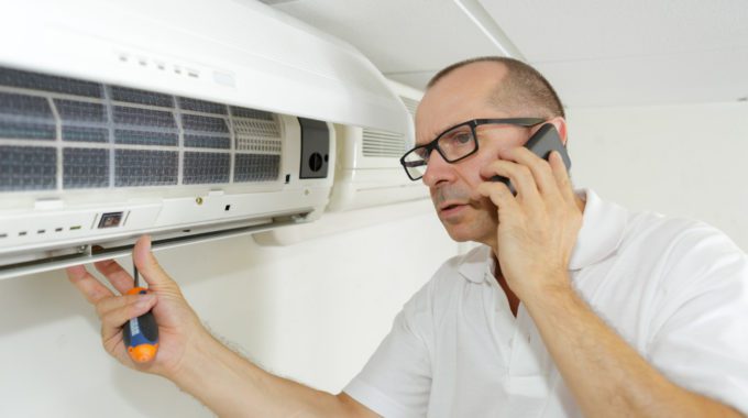 A Person Holding A Screwdriver And Talking On A Phone Beside The Ac